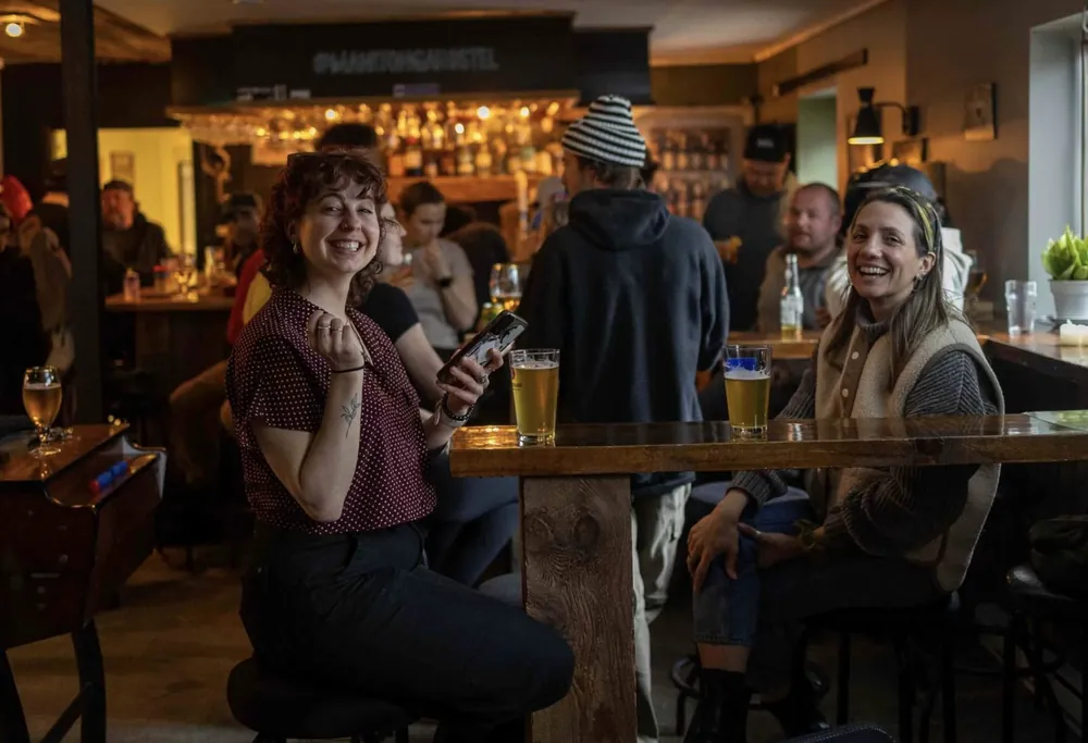Two friends smiling with beers at a high table in the busy bar
