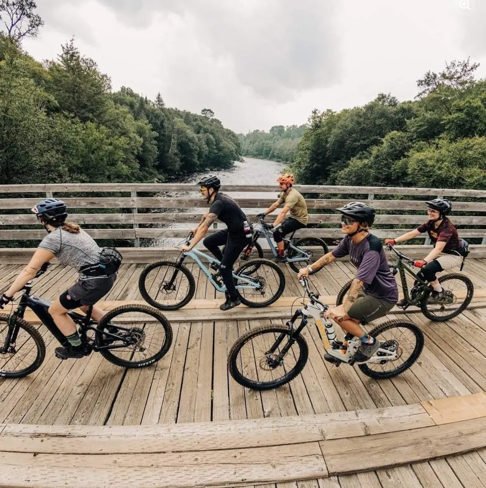 Group of mountain bikers riding across a wooden bridge over a river