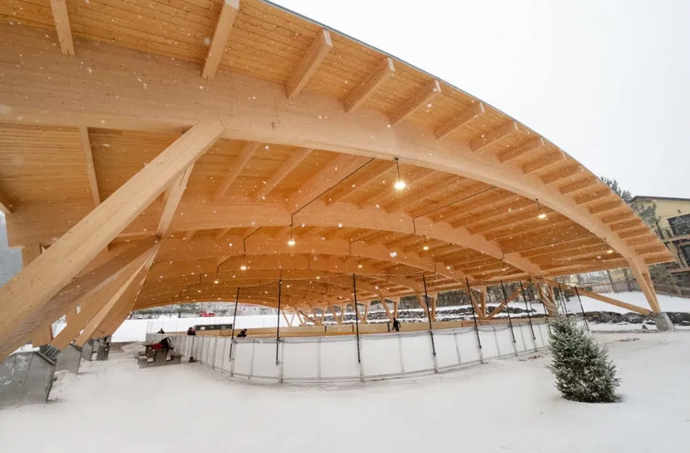 Outdoor skating rink under the curved wooden roof of the Parc Daniel-Lauzon pavilion, with snow falling