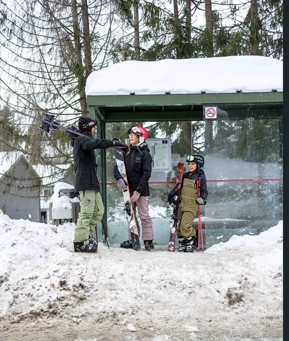 Family with skis waiting at the snowy bus shelter in the old village