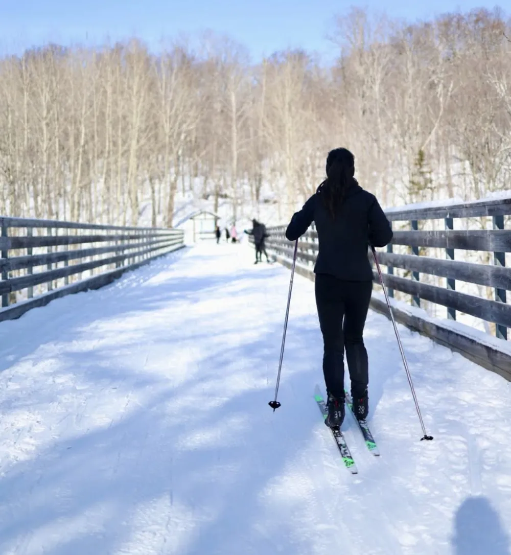 Cross-country skier crossing a snowy trail bridge on a sunny winter day